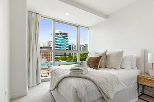 a bedroom with a white bed with a large window at Urban Escape Prime Location by Zodiak Stays in Auckland