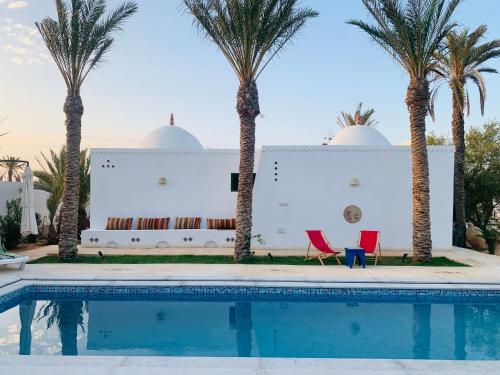 a pool with palm trees in front of a house at DIAR HAROUN in Djerba