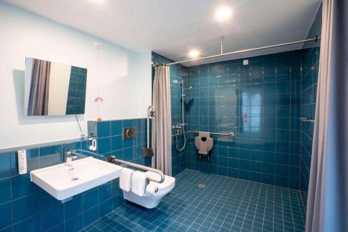 a blue tiled bathroom with a sink and a toilet at Prize by Radisson, Dresden Mitte in Dresden