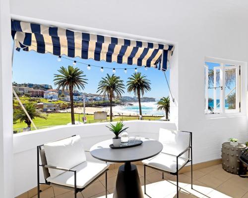 a table and chairs in front of a window with palm trees at Absolute Seafront Bronte in Sydney