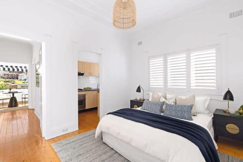 a white bedroom with a bed and a kitchen at Absolute Seafront Bronte in Sydney
