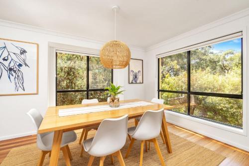 a dining room with a table and chairs and windows at Sandpiper, Hyams Beach in Hyams Beach