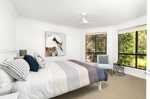 a white bedroom with a bed and two windows at Sandpiper, Hyams Beach in Hyams Beach
