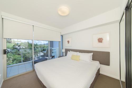 a bedroom with a white bed and a large window at Echelon Apartments Yeppoon in Yeppoon