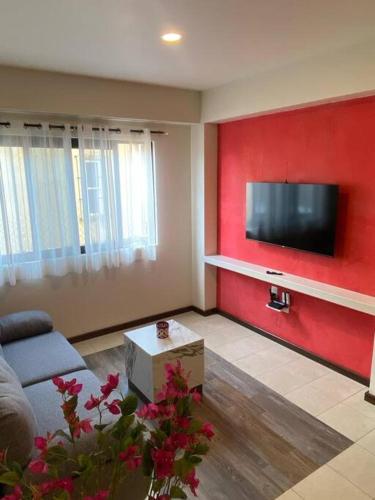 a living room with a red wall with a flat screen tv at Departamento Oaxaca Bella in Oaxaca City