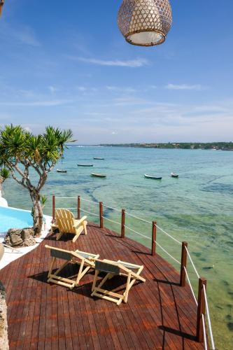 a bench and chairs sitting on a deck next to the water at Le Pirate Beach Club Nusa Ceningan - Adults Only in Nusa Lembongan