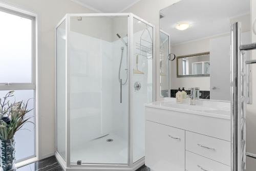 een witte badkamer met een douche en een wastafel bij Kaya-wai - Mangawhai Holiday Home in Mangawhai