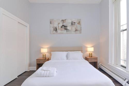 a white bedroom with a large bed and two lamps at Cozy Downtown Oasis in Hartford