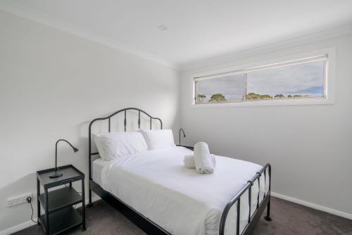 a white bedroom with a bed and a window at Shell Cove Escape in Shellharbour
