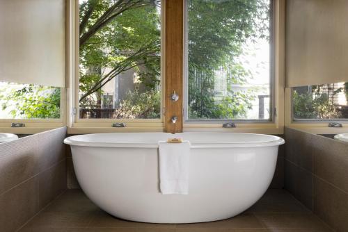 a large white bath tub in a bathroom with two windows at Mineral Springs Hotel Hepburn in Hepburn Springs