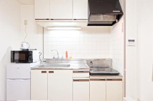 a white kitchen with a sink and a microwave at Shinjuku Waseda Earthtone Apartment in Tokyo