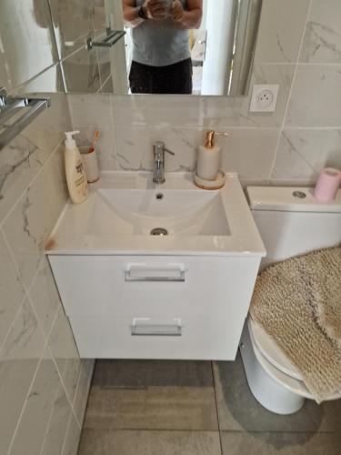 uma pessoa a tirar uma foto de um lavatório branco numa casa de banho em Chambre près de Walygator et Aqualand em Brax