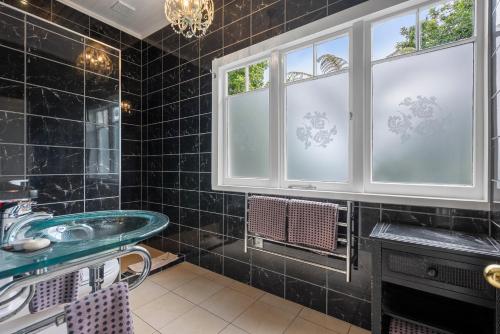 a black tiled bathroom with a sink and windows at Eden Park Bed And Breakfast Inn in Auckland