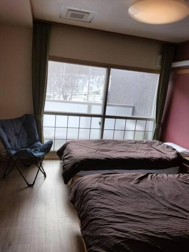 a bedroom with two beds and a chair and a window at フューディズコンドミニアム定山渓 in Jozankei