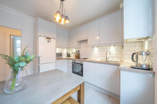 una cocina con armarios blancos y un jarrón de flores sobre una mesa en Charming 2 Bedroom Flat in Central London, en Londres