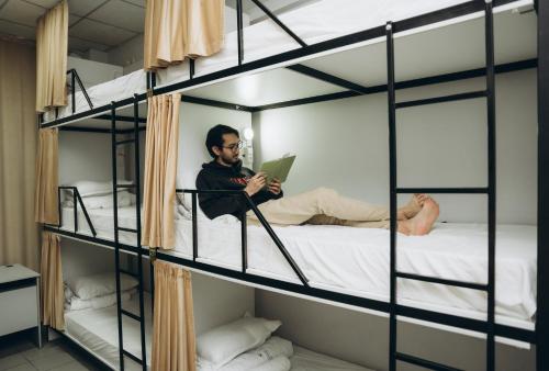 a man reading a book in a room with bunk beds at Sunny Hostel Nurmakova in Almaty