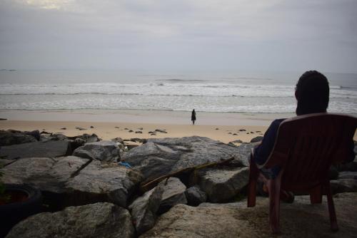 a man sitting in a chair looking out at the beach at WHITE SAND BEACH STAY- Delta hospitality- in Udupi
