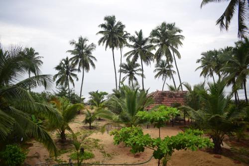 a group of palm trees on a beach with a building at WHITE SAND BEACH STAY- Delta hospitality- in Udupi