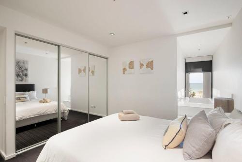 a white bedroom with a bed and a mirror at The Sandpiper Sanctuary at Henley Beach in Henley Beach South