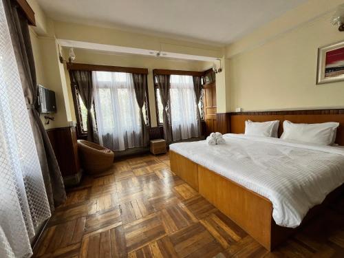 a bedroom with a large bed with white sheets and wooden floors at Yesheyzz in Gangtok