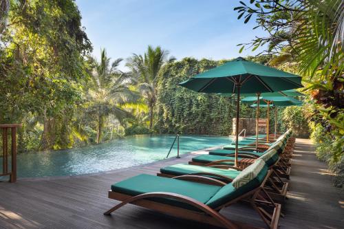 a row of lounge chairs with an umbrella next to a pool at Adiwana Unagi Suites in Ubud