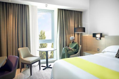 a man sitting in a chair in a hotel room at Novotel Muscat Airport in Muscat