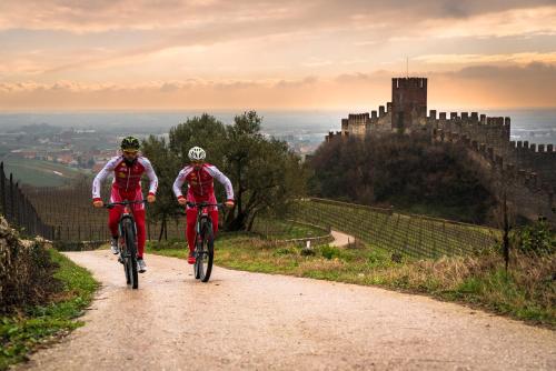 two people riding bikes down a dirt road with a castle in the background at Nice and cozy appartment Innside photos are coming soon in Dogliani