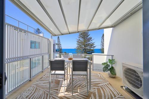 a patio with a table and chairs on a balcony at Dwell @ 25, Oceanfront Apartment in Bargara