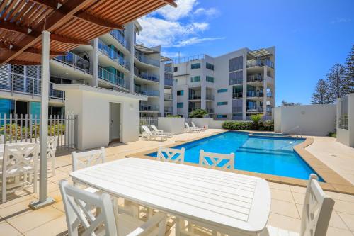 a patio with a table and chairs next to a swimming pool at Dwell @ 25, Oceanfront Apartment in Bargara