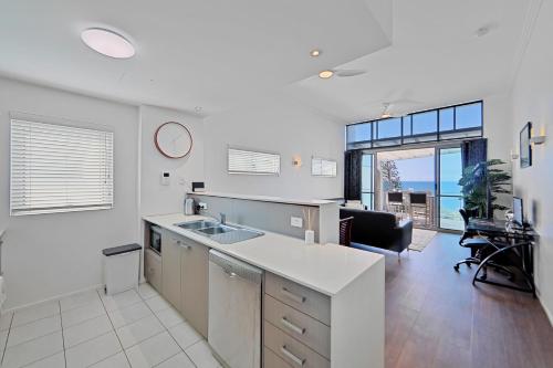a kitchen with a sink and a living room at Dwell @ 25, Oceanfront Apartment in Bargara