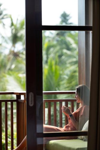 a woman sitting on a balcony looking out a window at Adiwana Unagi Suites in Ubud