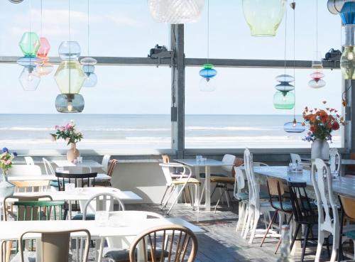 un restaurante con mesas y sillas y vistas al océano en Villa de Duinfazant en Bergen aan Zee