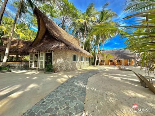 a building with a thatched roof and palm trees at Coco Grove Beach Resort, Siquijor Island in Siquijor