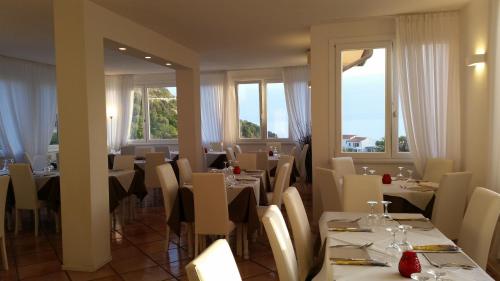 a restaurant with tables and white chairs and windows at Hotel L'Ogliera in Pomonte