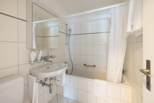 a white bathroom with a sink and a bath tub at EMA House Serviced Apartments Aussersihl in Zürich