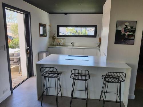 une cuisine avec un comptoir et trois tabourets de bar dans l'établissement MAISON CONTEMPORAINE à 5KM DE BIARRITZ AVEC JACUZZI, à Bassussarry
