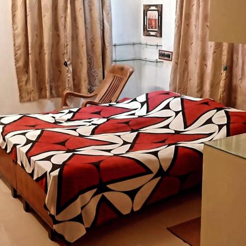 uma cama com um cobertor vermelho e branco e uma cadeira em Parthasarathy Home stay em Trivandrum