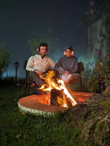 two men sitting around a fire in the grass at Cloudwalks Homestay in Kodaikānāl