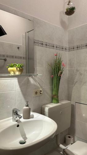 La salle de bains est pourvue d'un lavabo, de toilettes et d'un vase de fleurs. dans l'établissement Nord Ost Apartment, à Kiel
