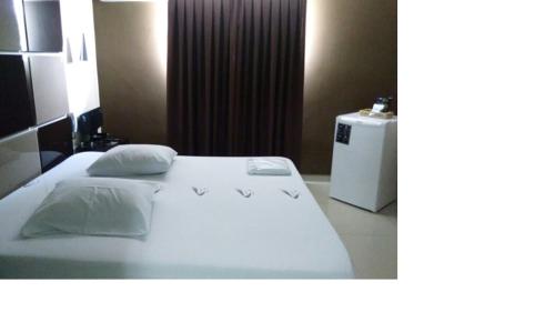 a bedroom with a white bed with two pillows and a refrigerator at Minuty Motel Itu in Itu
