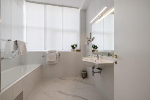 a white bathroom with a sink and a tub and a mirror at Art Hotel in Split
