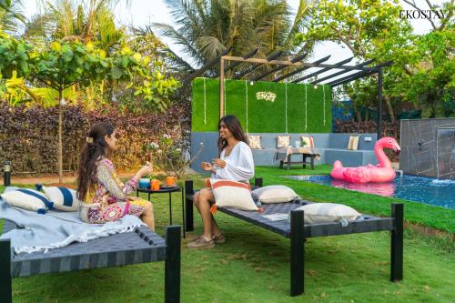 two girls sitting on beds in a garden with a pool at EKO STAY- PANORAMA VILLA in Alibaug