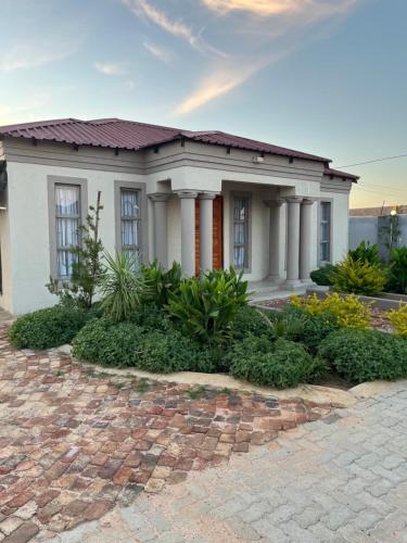 a small white house with columns on a brick driveway at Mafikeng Boutique Lodge in Mahikeng