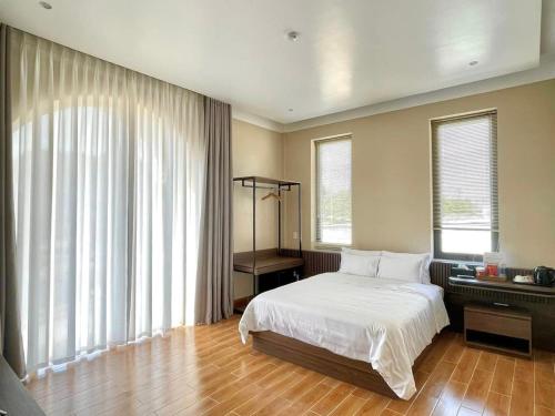 a bedroom with a bed with white sheets and windows at MELA HOTEL in Mỹ Thạch