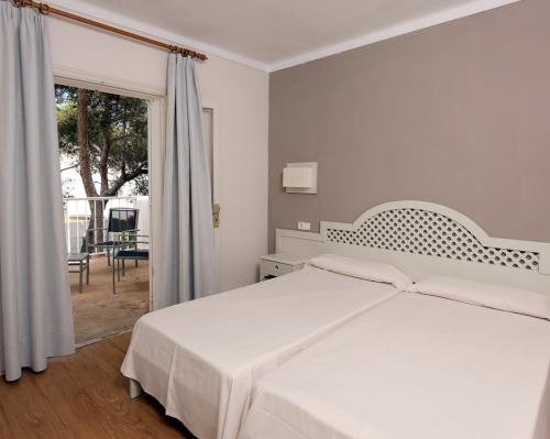 a white bedroom with a bed and a balcony at Hotel Club Es Talaial in Cala d´Or