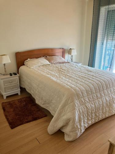 a bedroom with a bed with a white comforter and a window at Sol da Caparica in Costa da Caparica