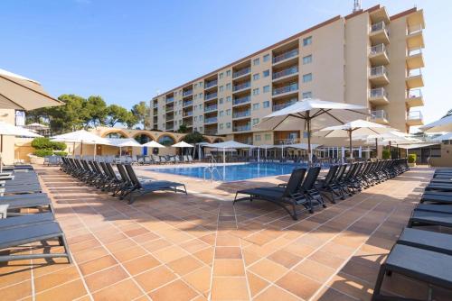 uma piscina com cadeiras e guarda-sóis ao lado de um hotel em Hotel Atlantic by Hoteles Centric em Es Cana