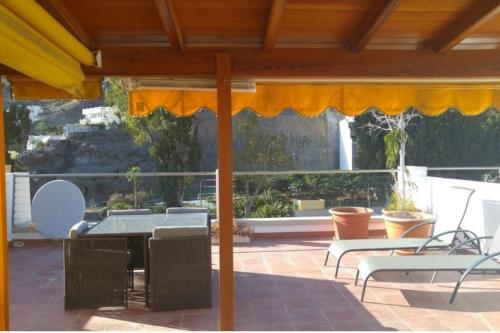 a patio with a table and chairs and an umbrella at Paraíso con gran solarium privado en playa Mogán in Puerto de Mogán