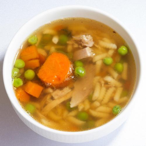 a white bowl of soup with carrots and peas at Simbad Hotel & Bar Superior in Mosonmagyaróvár