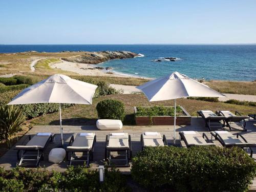 een groep stoelen en parasols naast de oceaan bij Sofitel Quiberon Thalassa sea & spa in Quiberon